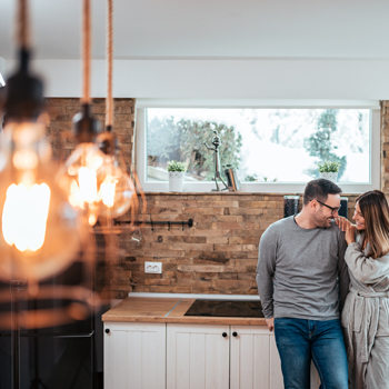 smiling couple in modern neutral kitchen behind close up of industrial hanging light bulbs