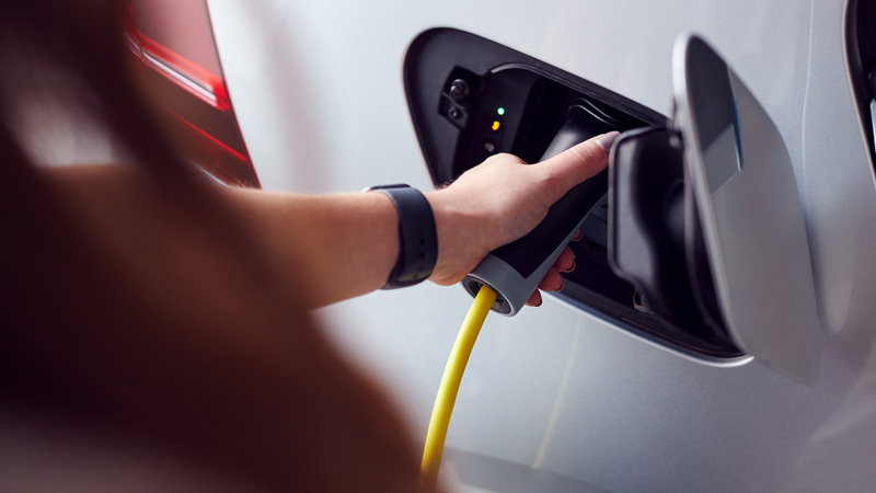 close up of womans hand plugging in white electric vehicle to charge